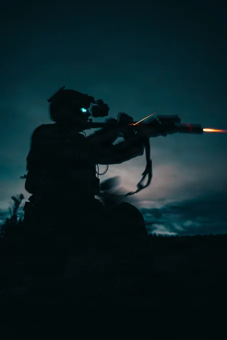 Green beret firing a weapon at night. all you can see are the lights on his goggles and the fire from the gun. 