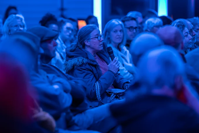 A photo of an audience member at an event, asking a question while holding a microphone