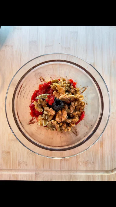Tabla de madera con los ingredientes para una versión rápida de muhammara: pimientos del piquillo, nueces, ajo, lima, especias y aceite de oliva virgen extra. Los ingredientes están colocados antes de triturarlos para preparar la crema.