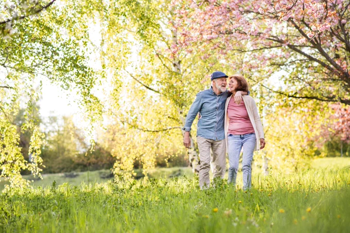 Couple walking arm in arm through a sunlit meadow with blooming trees in springtime.