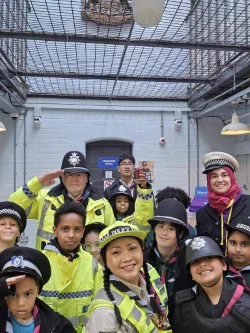 A diverse group of children and adults, many dressed as police officers, smiling for a photo in a museum.