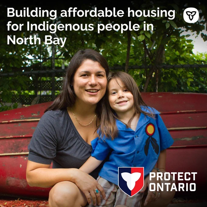 Indigenous mother and daughter smile in front of an upturned boat. Text reads: Building affordable housing for Indigenous people in North Bay