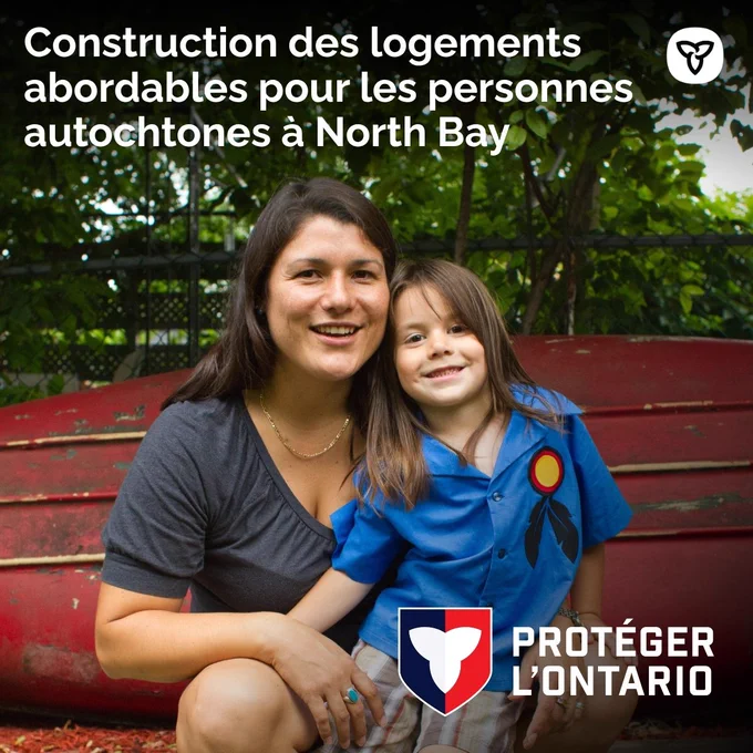 Une mère et sa fille autochtones sourient devant un bateau renversé. Texte : Construction des logements abordables pour les personnes autochtones à North Bay
