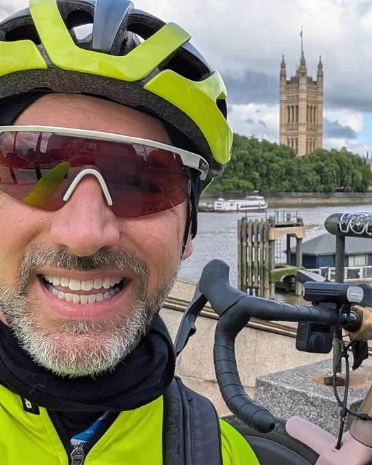 A close-up portrait of a smiling cyclist wearing a helmet and sunglasses.
