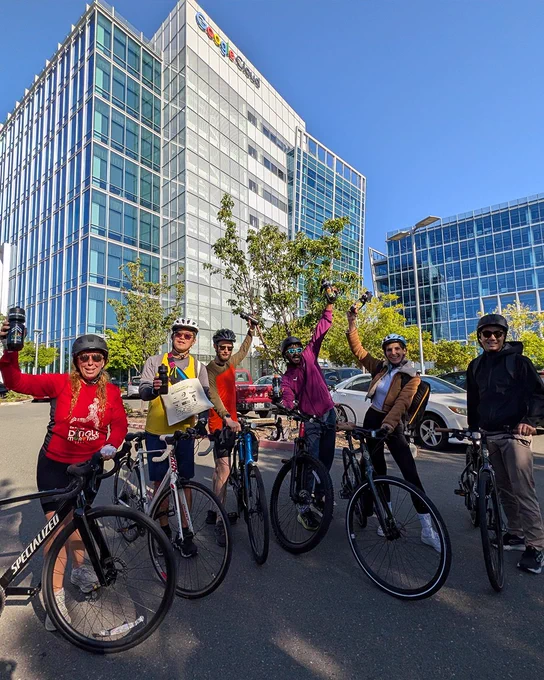 A group of six colleagues smiling and posing while seated on their bicycles.
