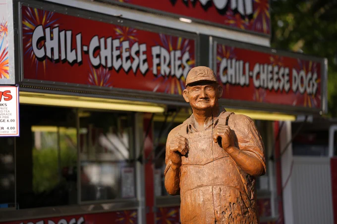A wooden Statue of a farmer in overalls in front of a food stand at the Iowa State Fair.