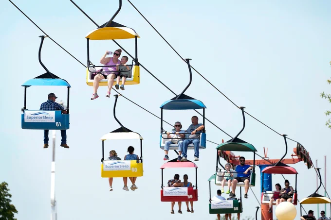 people on a the skygliders. The photo is taken from the ground so the background is a light blue sky with no clouds.
