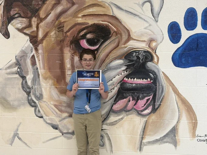 Evan Hup in front of bulldog mural holding a certificate