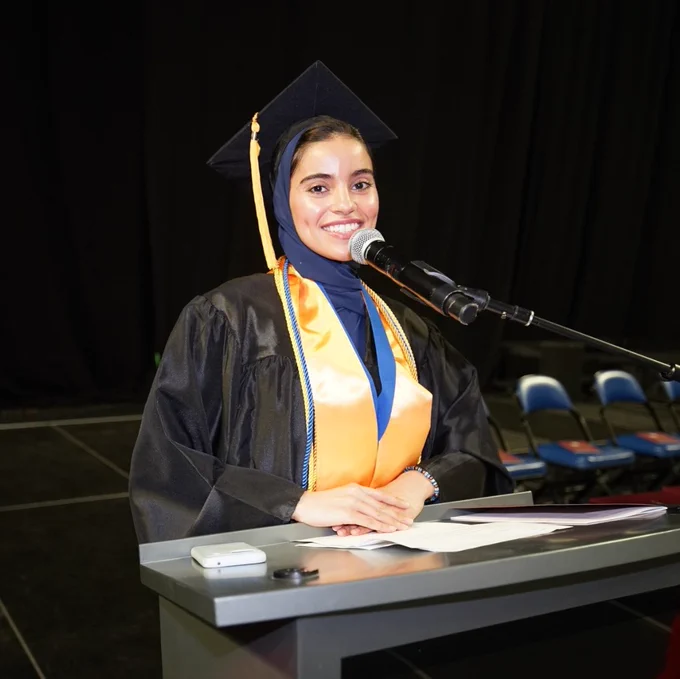 Female graduate stands at podium as she delivers a speech at graduation.