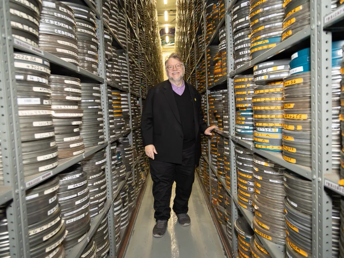 A man, posing for a photo, stood between two storage racks holding hundreds of film cans.
