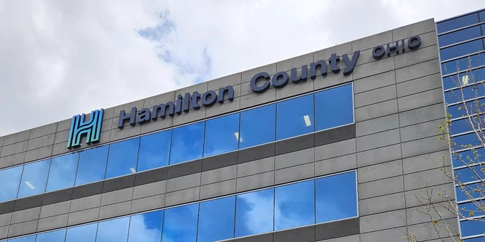 Modern multi-story office building with dark exterior panels and large reflective windows, featuring the Hamilton County, Ohio name and stylized “H” logo near the roofline.