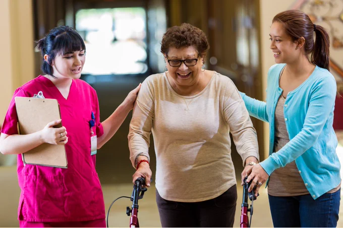 Two women helping a woman with a walker move forward.
