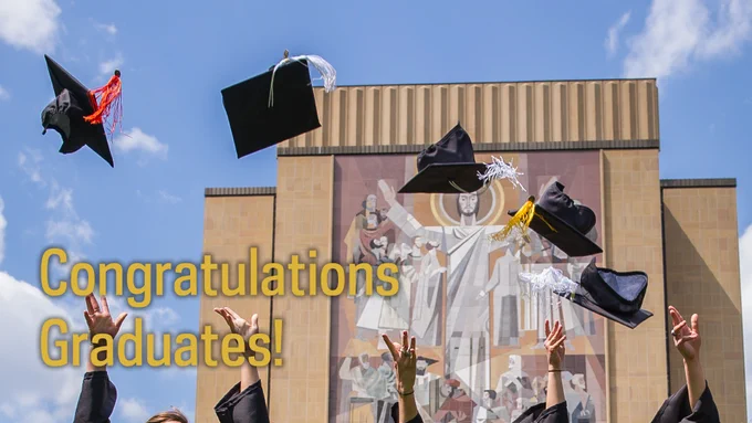 Hands of students can be seen along the bottom, throwing their black graduation caps in the air. In the background is the Word of Life mural on Hesburgh Library.