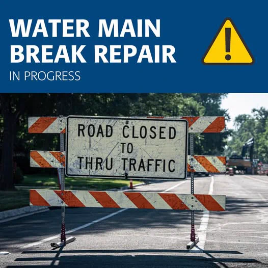 Water main break repair in progress. Photo of a road closure sign blocking traffic on a street. 