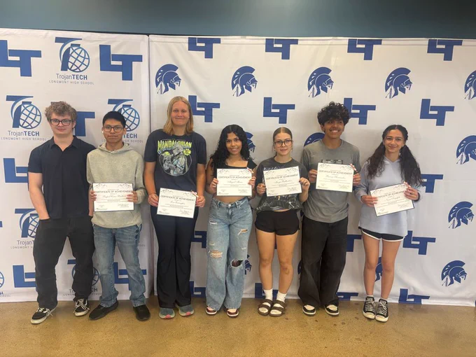 Seven high school students stand in a row in front of a TrojanTech Longmont High School step-and-repeat banner, each holding a Certificate of Achievement.