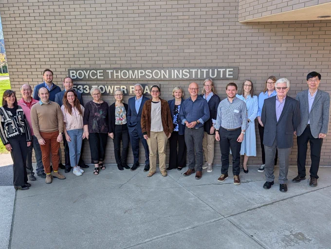 A group of BTI Board of Directors members, faculty, and staff stand together outside the Boyce Thompson Institute building in front of the institute’s sign. The group poses on a sunny day along the building’s brick exterior during the Board’s campus visit.