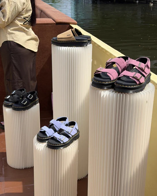 An image of four pairs of Dr Martens sandals sitting on white podiums next to a canal.