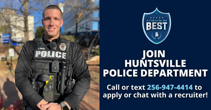 A uniformed Huntsville Police Department officer stands outdoors in a landscaped area with buildings, trees, and signage in the background. The officer is wearing a black police vest with visible equipment, including a radio, camera, and duty gear. On the right side of the image, a dark blue graphic displays a badge‑shaped logo reading “A Call to Be the Best” above the text “Join Huntsville Police Department. Call or text 256‑947‑4414 to apply or chat with a recruiter.”