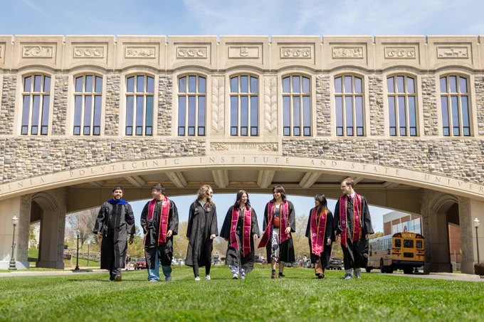 Seven Virginia Tech graduates in their graduation gowns in front of Torg Bridge. 