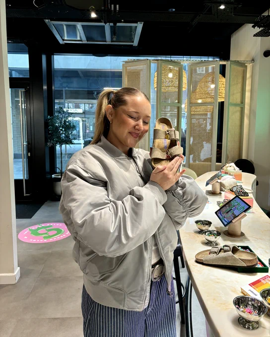 An image of a person holding a taupe BIRKENSTOCK Boston sandal whilst standing at a nail bar.