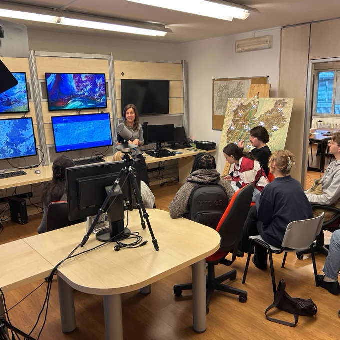UA Water-R20 NRT students attend a presentation by meteorologist Erica Cova at Meteotrentino weather forecast center in Trento, Italy, with recording equipment and forecast displays visible in the operational forecasting room.