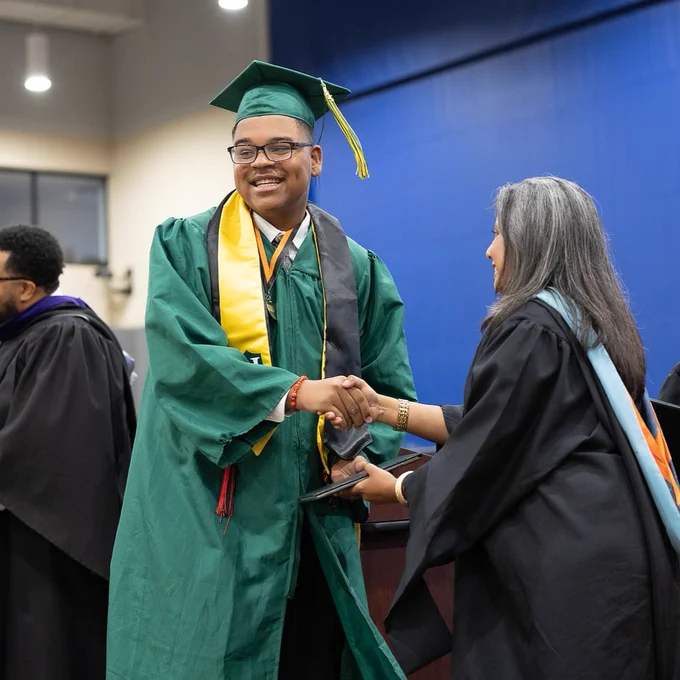 A Henrico High School graduate smiles while shaking hands and receiving his diploma from his principal at the 2025 graduation ceremony at the Henrico Sports & Events Center.