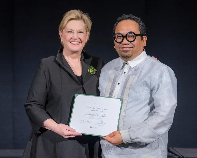 Ohio University President Lori Stewart Gonzalez and Adonis Durado stand together smiling with a certificate in front of a black curtain.