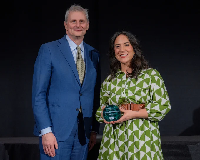 Ohio University Executive Vice President and Provost Donald Leo and Candice Rios Wenmoth stand together smiling with an award in front of a black curtain.