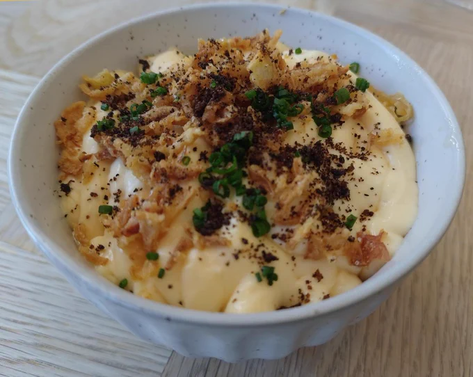 A small round dish containing lightly smoked Jersey Royal potatoes, cheese custard, onions in various guises (soubise, pickled), topped with crispy onions and leek ash