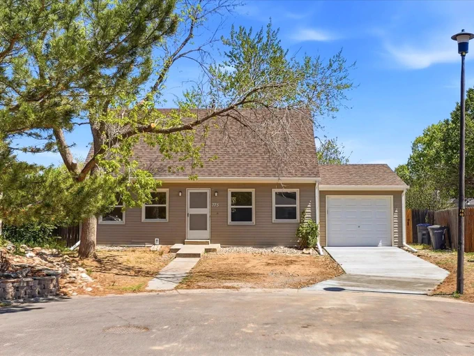 Single-story beige house with a sloped roof, attached garage, and a concrete driveway under a clear blue sky.