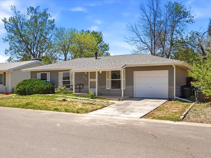Single-story suburban house with a gray exterior, attached garage, and a small front porch under a clear blue sky.
