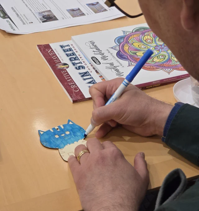 Close-up on the hands of a man as he colors in a wooden cat with a magic marker
