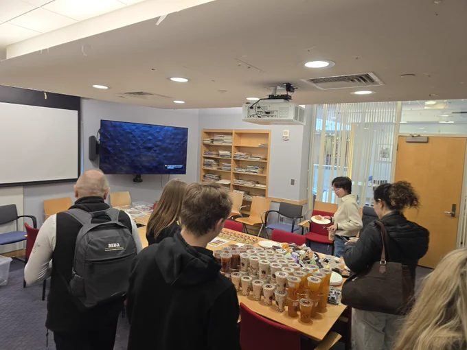A bund of people stand around a conference room table that is stacked with boba teas