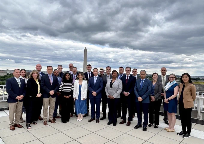 Members from BOEM, BSEE, and the U.S. Army War College stand together for a group photo. The National Monument stands behind them and dark gray clouds hover dramatically above them.