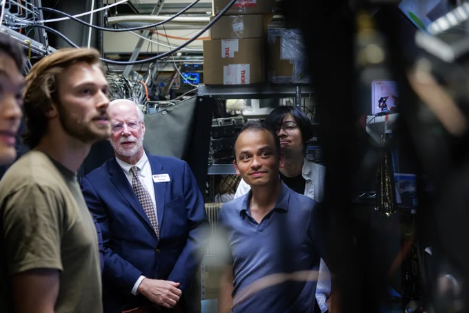 A group of people observe complex machinery and electronic equipment in a research laboratory.
