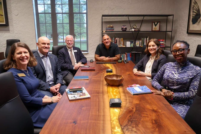 JB Holston and Chancellor Justin Schwartz sit with four other professionals around a large wooden conference table in a modern office with bookshelves and framed art on the walls.