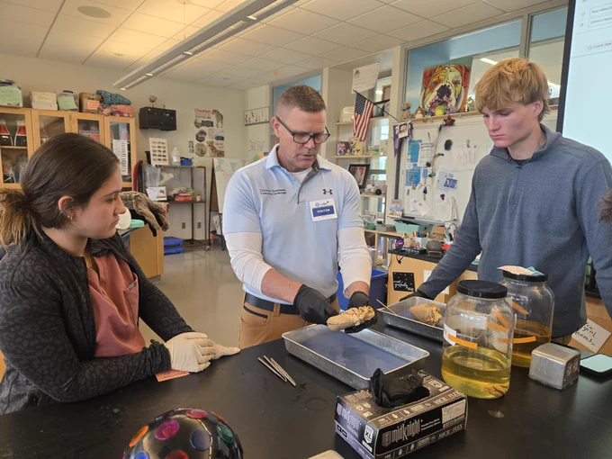Three gathered around a table, engaged in a hands-on STEM activity involving Dr. Kevin Christiansen sharing veterinary cardiology dissection of a pig's heart with CAPS Veterinary medicine students.