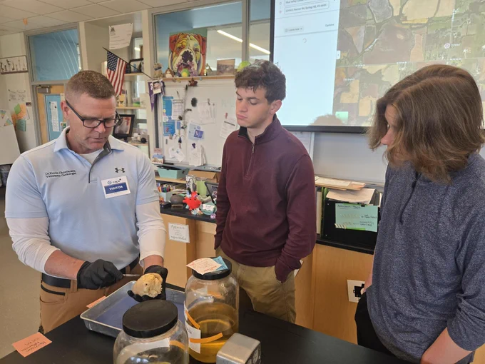 Three people, two students and Dr. Kevin Christiansen, working together in a classroom setting, with him showing them how to dissect a pig's heart and learning about animal anatomy.