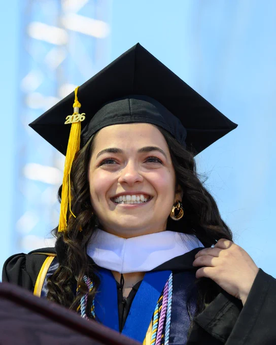 Gulsinam Akhmadzhanova, wearing a graduation cap and gown and smiling while standing at the podium."