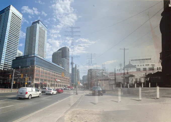 Modern city street with tall glass skyscrapers and cars driving under a partly cloudy sky layered over a historic black and white image.