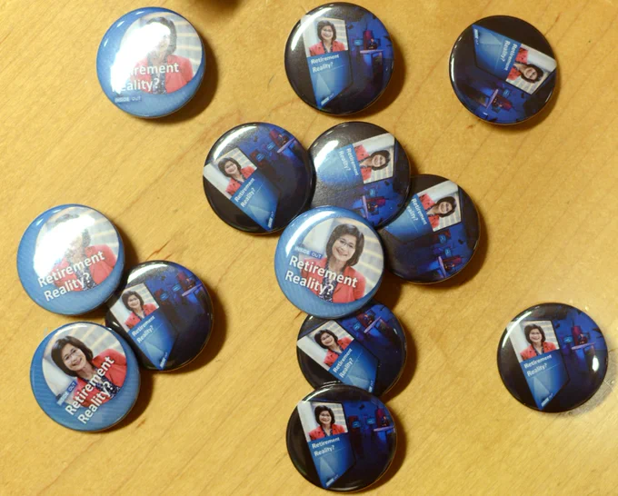 A small pile of Susan Han buttons. The buttons are part of a Seattle Channel tradition for departing staff members. The buttons are blue and include a photo of Susan Han, who is wearing a bright red jacket, and button reads "Retirement Reality?"
