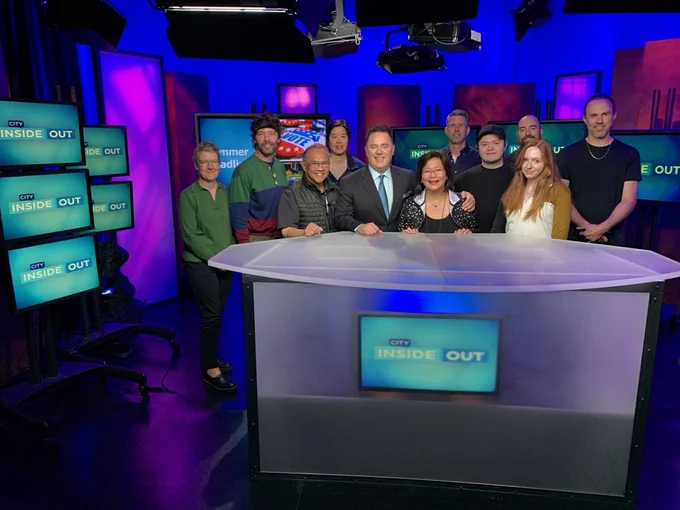 Seattle Channel staff and the City Inside/Out production crew pose for a photo following Susan Han’s final show as senior producer. Several blue television monitors appear in the background against a purple studio backdrop.