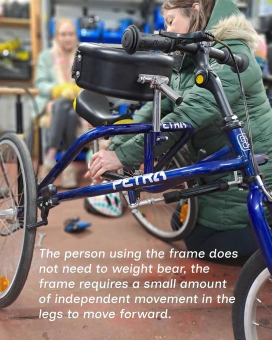 A photo of a blue child frame runner in a workshop with the text stating 'The person using the frame does not need to weight bear, the frame requires a small amount of independent movement in the legs to move forward.'