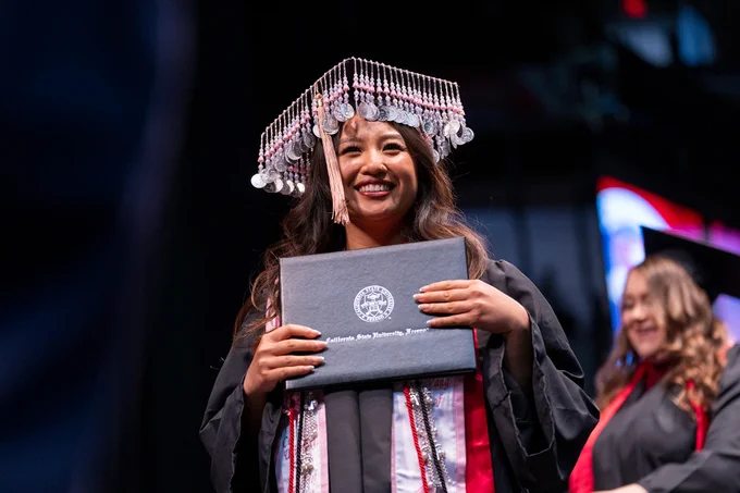 A graduate in traditional Hmong regalia holds her diploma with pride.