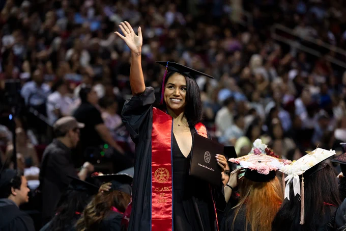 A graduate waves to loved ones after receiving her diploma.