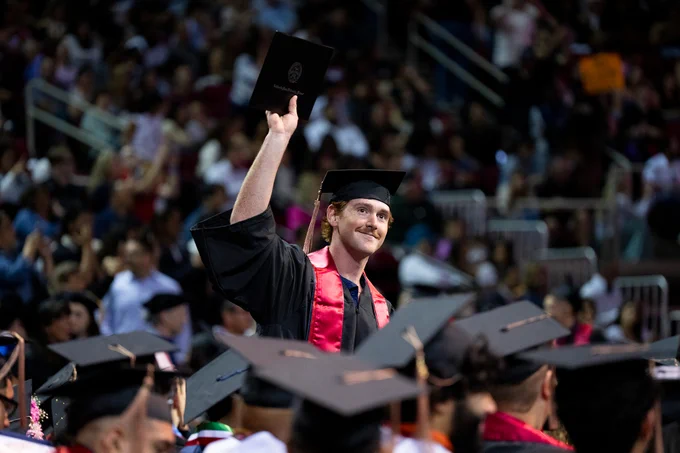 A graduate raises his diploma into the air in celebration during commencement.