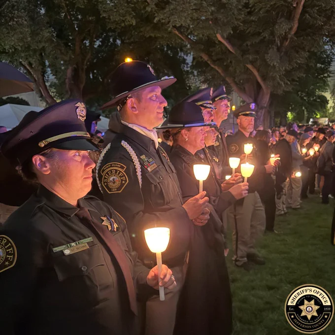 Uniformed sheriff’s office members stand in formation at dusk holding glowing candles during a memorial vigil. A Jefferson County Sheriff’s Office logo appears in the bottom-right corner.