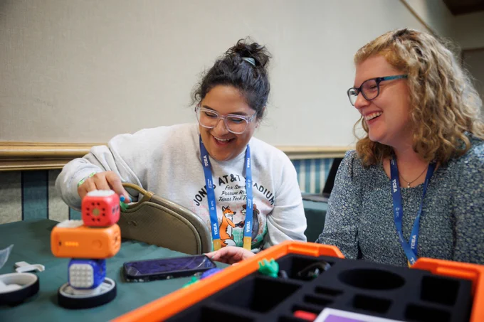 Photo of two people smiling while participating in an activity at a table. 