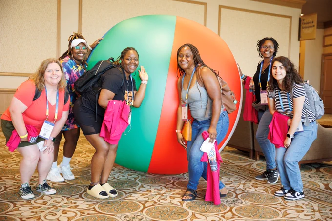 Photo of a group of people smiling and posing in front of a huge beach ball. 