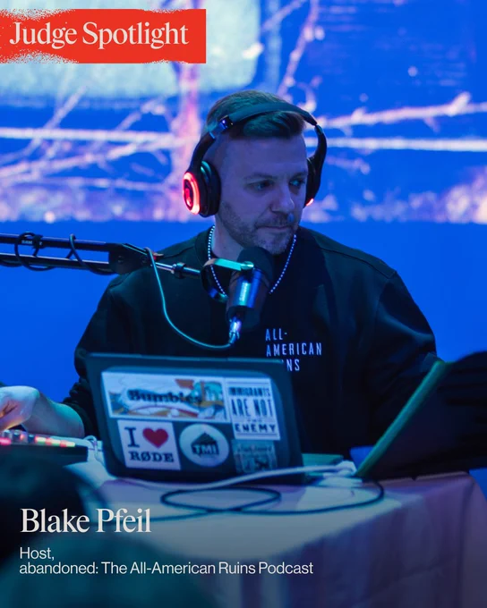 A podcast host sits at a table with a laptop and microphone, wearing headphones with a blue background. The setting has a focused and professional atmosphere.